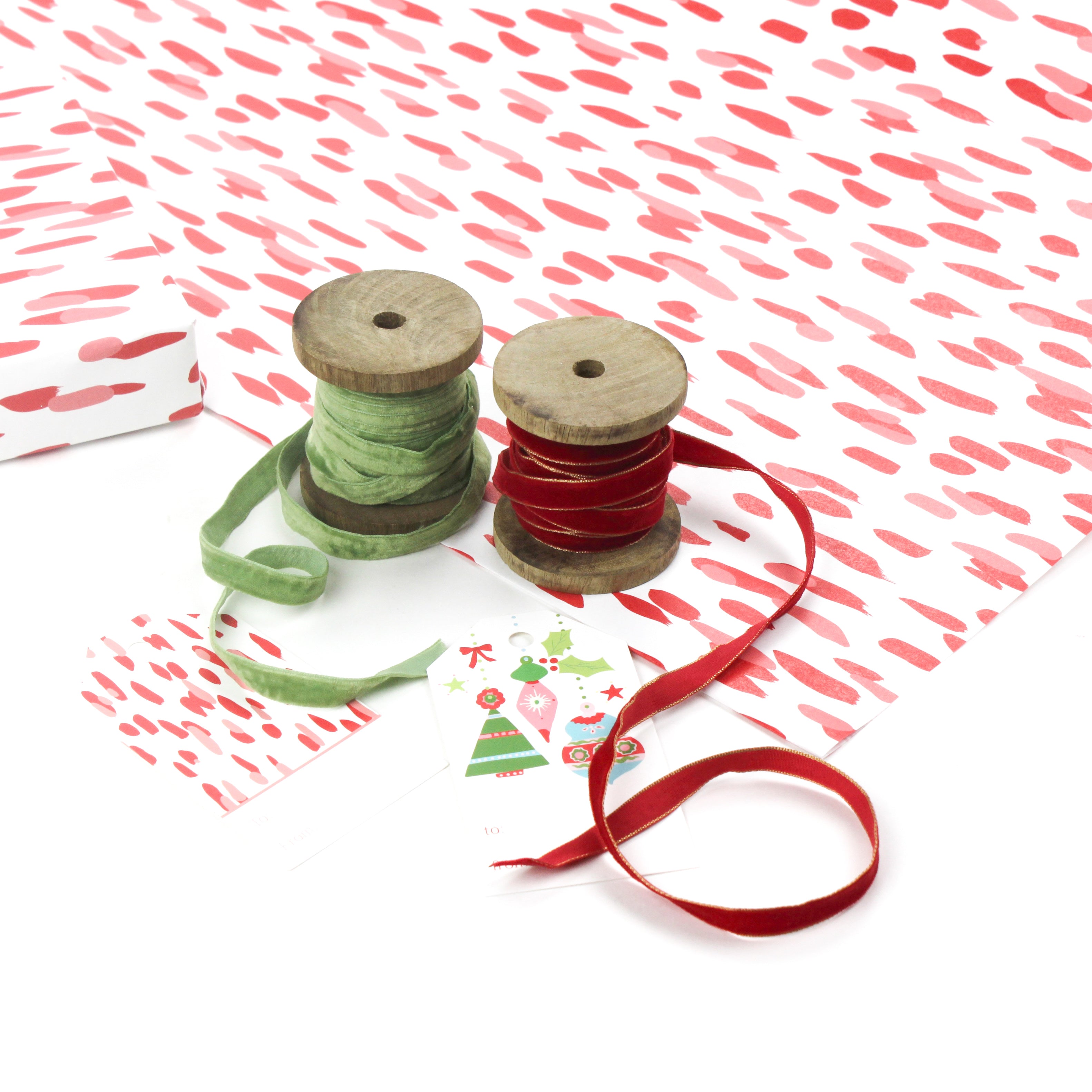 Styled display of red brushstroke wrapping paper with ribbons and holiday gift tags.