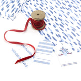 Styled Club House blue wrapping paper with hand-painted abstract pattern, shown with ribbon spool and coordinating gift tags 