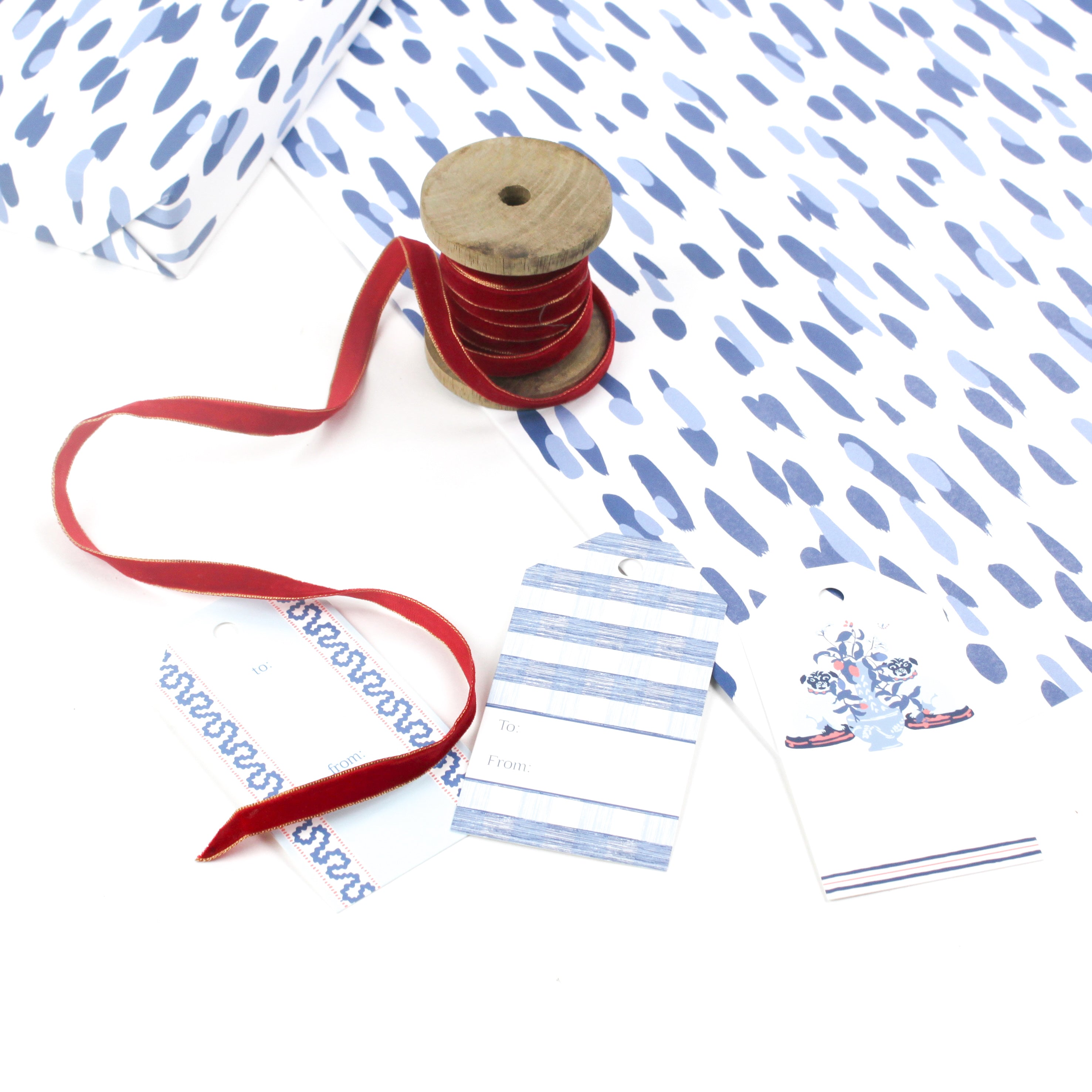 Styled Club House blue wrapping paper with hand-painted abstract pattern, shown with ribbon spool and coordinating gift tags 