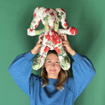 White stuffed elephant toy with red and green floral pattern and green bow held by a lady.