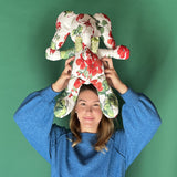 White stuffed elephant toy with red and green floral pattern and green bow held by a lady.