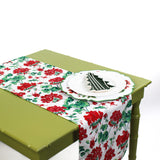 Floral table runner on a green table styled with layered decorative plates.