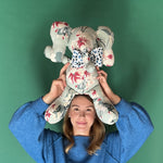 Floral patterned stuffed elephant toy with a blue and white bow held by a girl with green background.