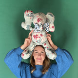 Floral patterned stuffed elephant toy with a blue and white bow held by a girl with green background.