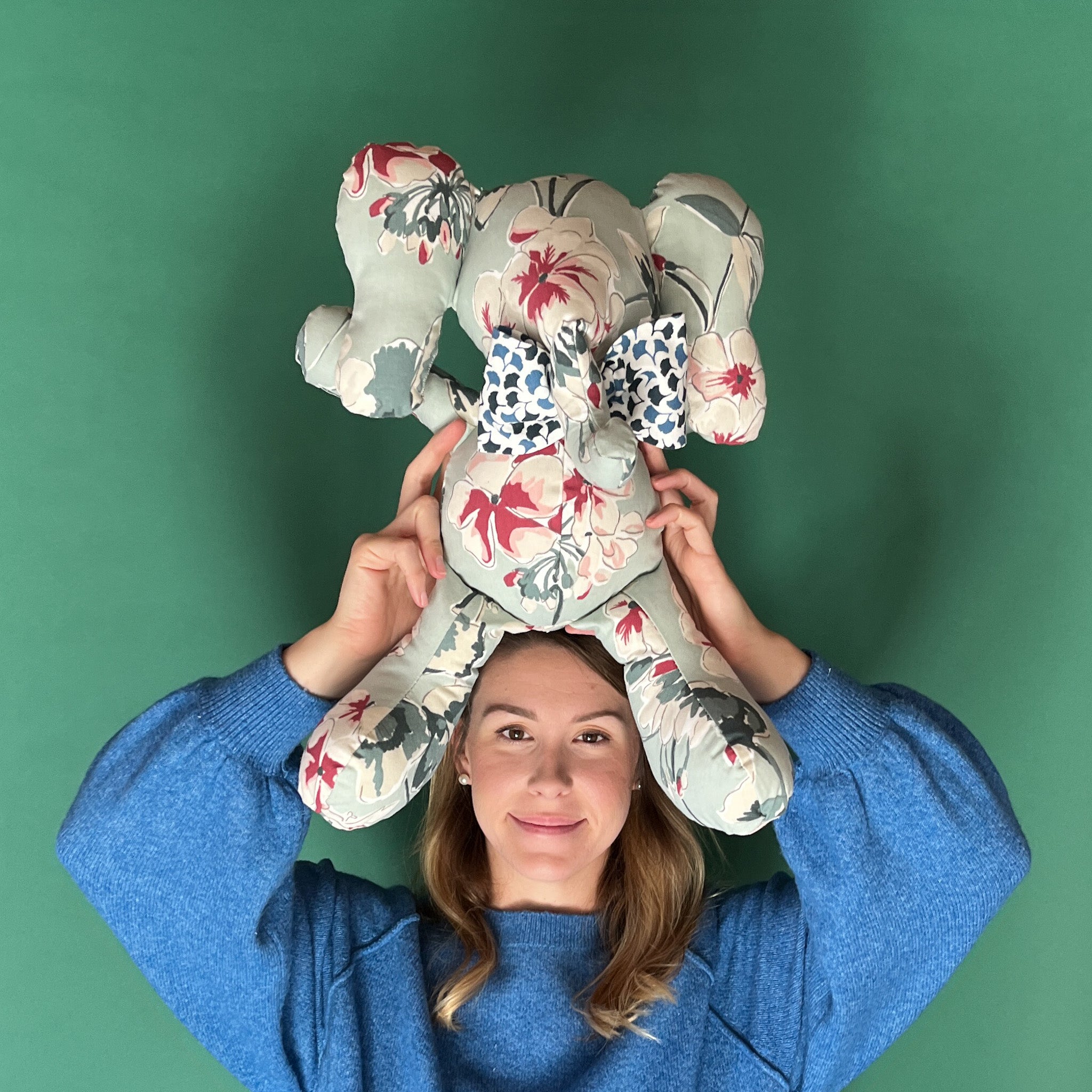 Floral patterned stuffed elephant toy with a blue and white bow held by a girl with green background.