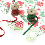 Styled display of red geranium wrapping paper with green and red ribbons and assorted gift tags.