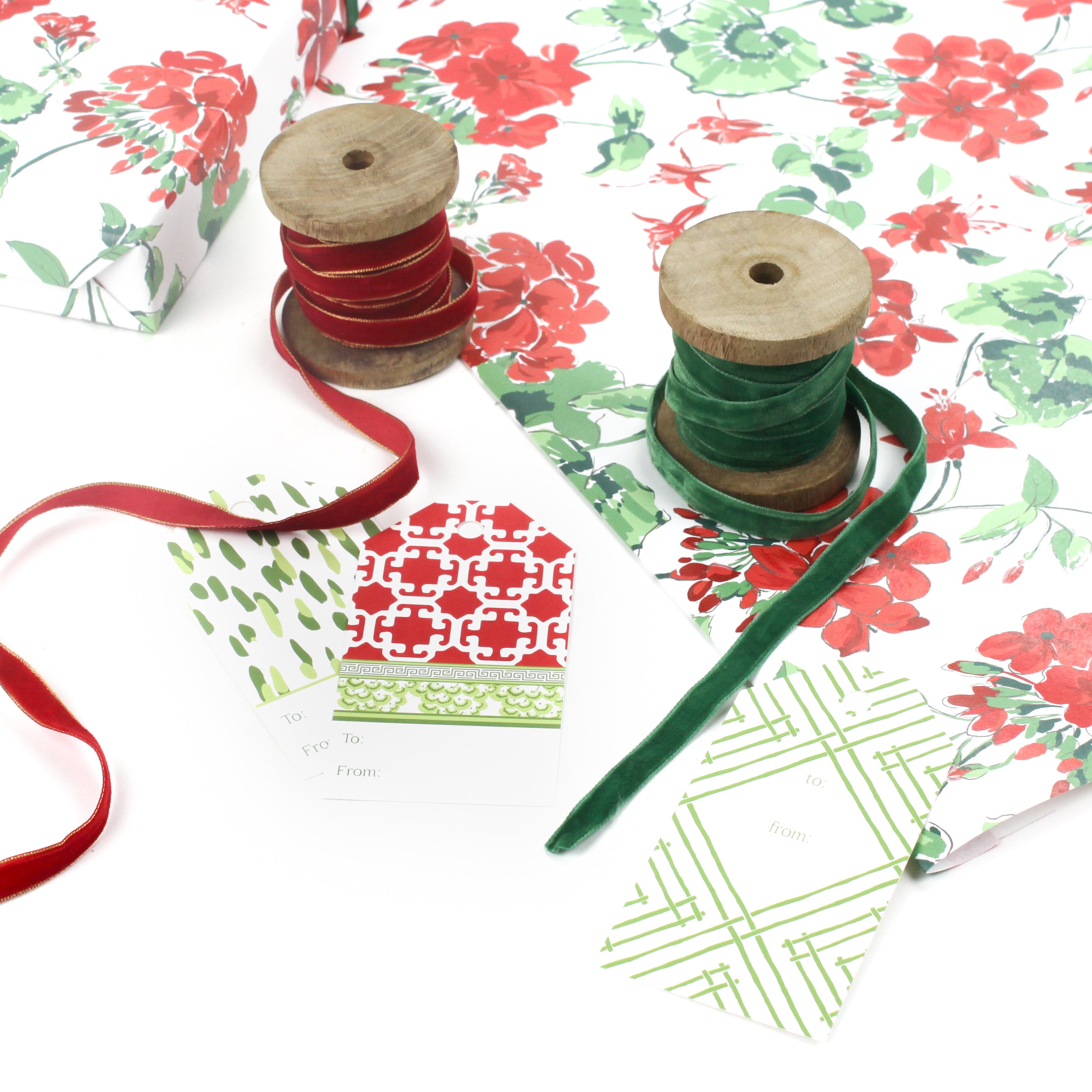 Styled display of red geranium wrapping paper with green and red ribbons and assorted gift tags.