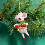 A felt mouse ornament wearing a green scarf and hat holds a red bow with a small gold bell hanging from it.