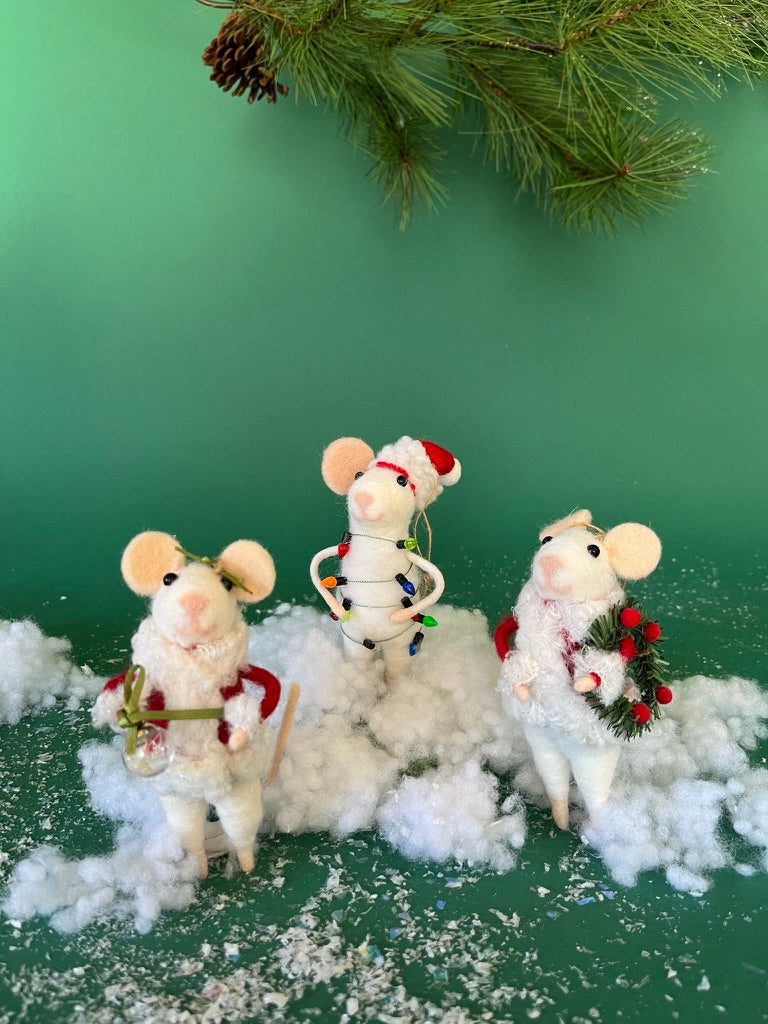 Three white felt mouse ornaments dressed in cozy winter outfits, one wrapped in colorful holiday lights, one holding a Christmas wreath, and one holding a festive ornament