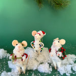Three white felt mouse ornaments dressed in cozy winter outfits, one wrapped in colorful holiday lights, one holding a Christmas wreath, and one holding a festive ornament