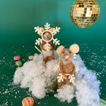 Two felt mouse ornaments dressed as snowflakes stand on fake snow beneath a gold disco ball, surrounded by scattered candy on a green background.