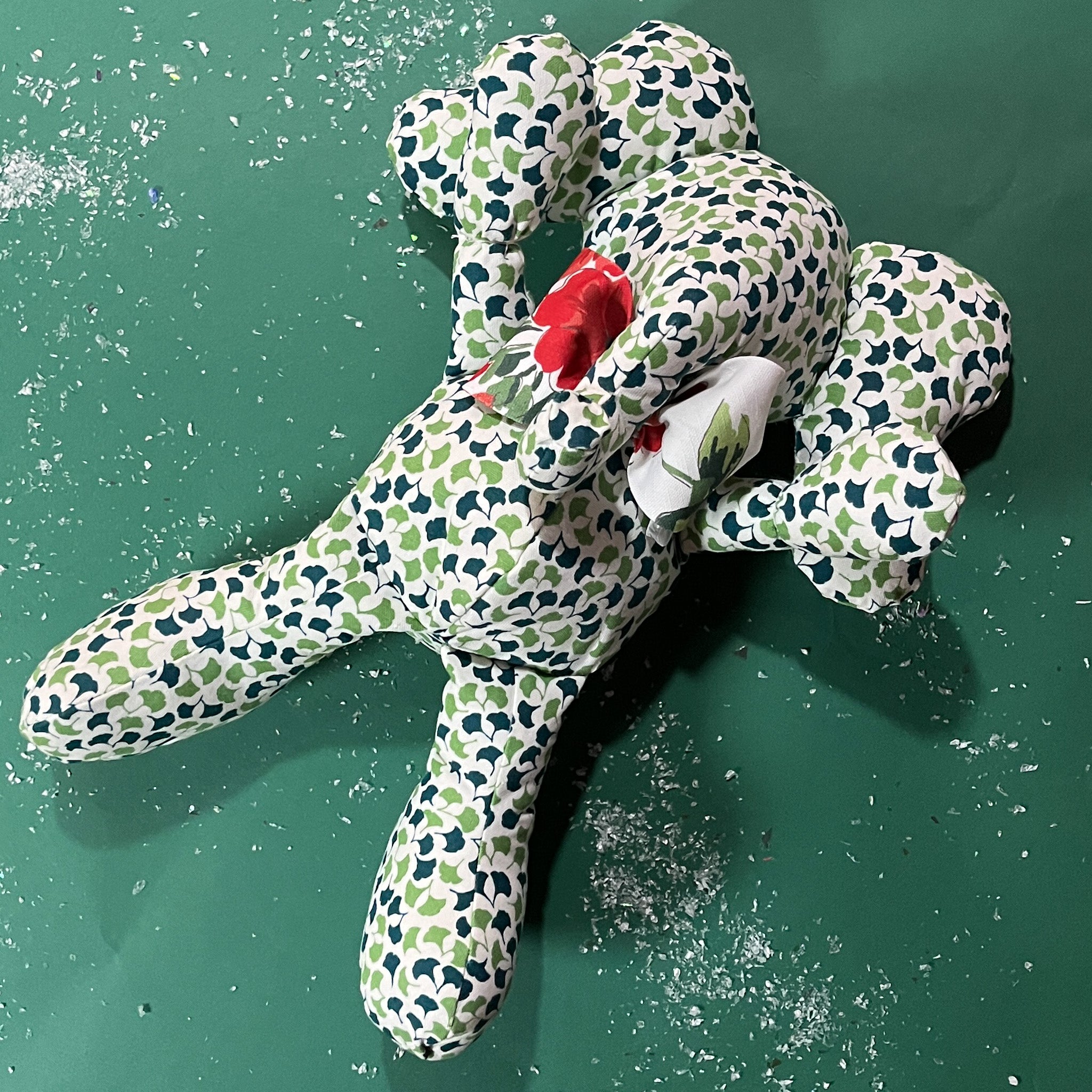 Green and white patterned stuffed elephant toy with a red bow in a green background.