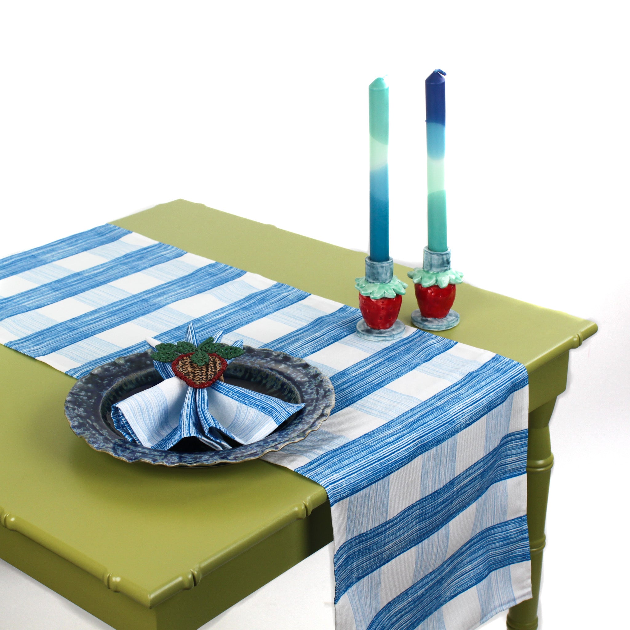 Styled blue and white checkered table runner on a green table with candles and a decorative place setting.