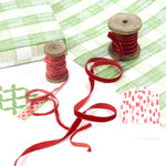 Styled flat lay of green gingham wrapping paper with red velvet ribbon on wooden spools, decorative gift tags, and a wrapped box, shown as everyday gift wrap inspiration.