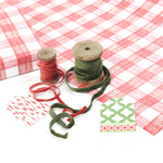 Red and white gingham Christmas wrapping paper displayed with ribbon spools and gift tags.