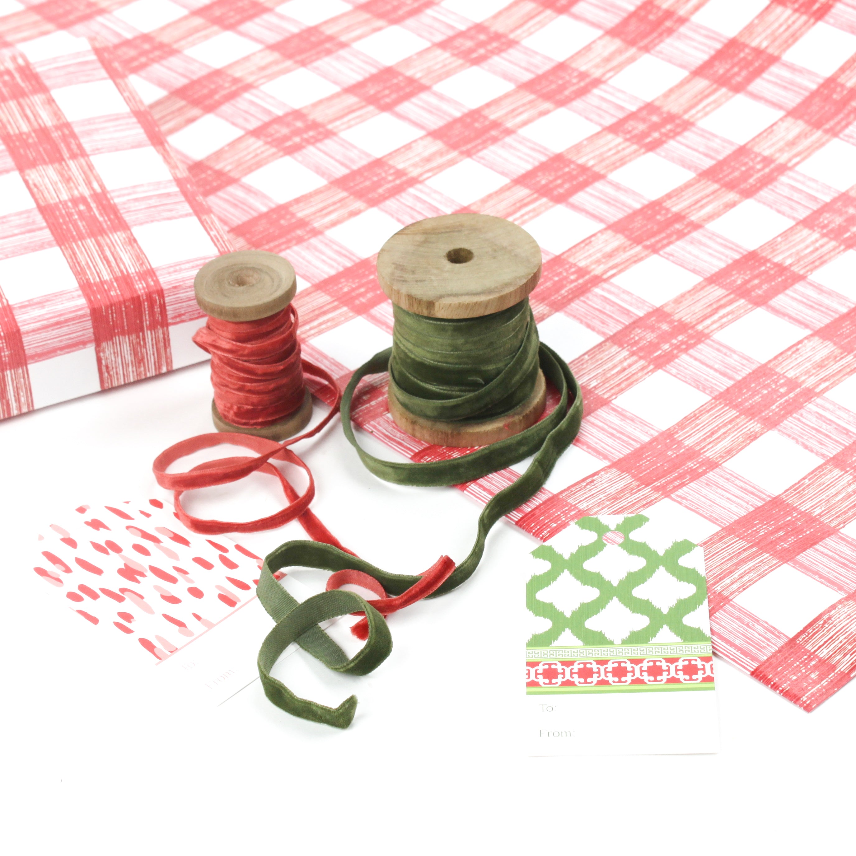 Red and white gingham Christmas wrapping paper displayed with ribbon spools and gift tags.