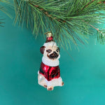 Christmas pug ornament of a dog in a red outfit hanging on a pine branch.