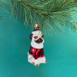 Christmas pug ornament of a dog in a red outfit hanging on a pine branch.
