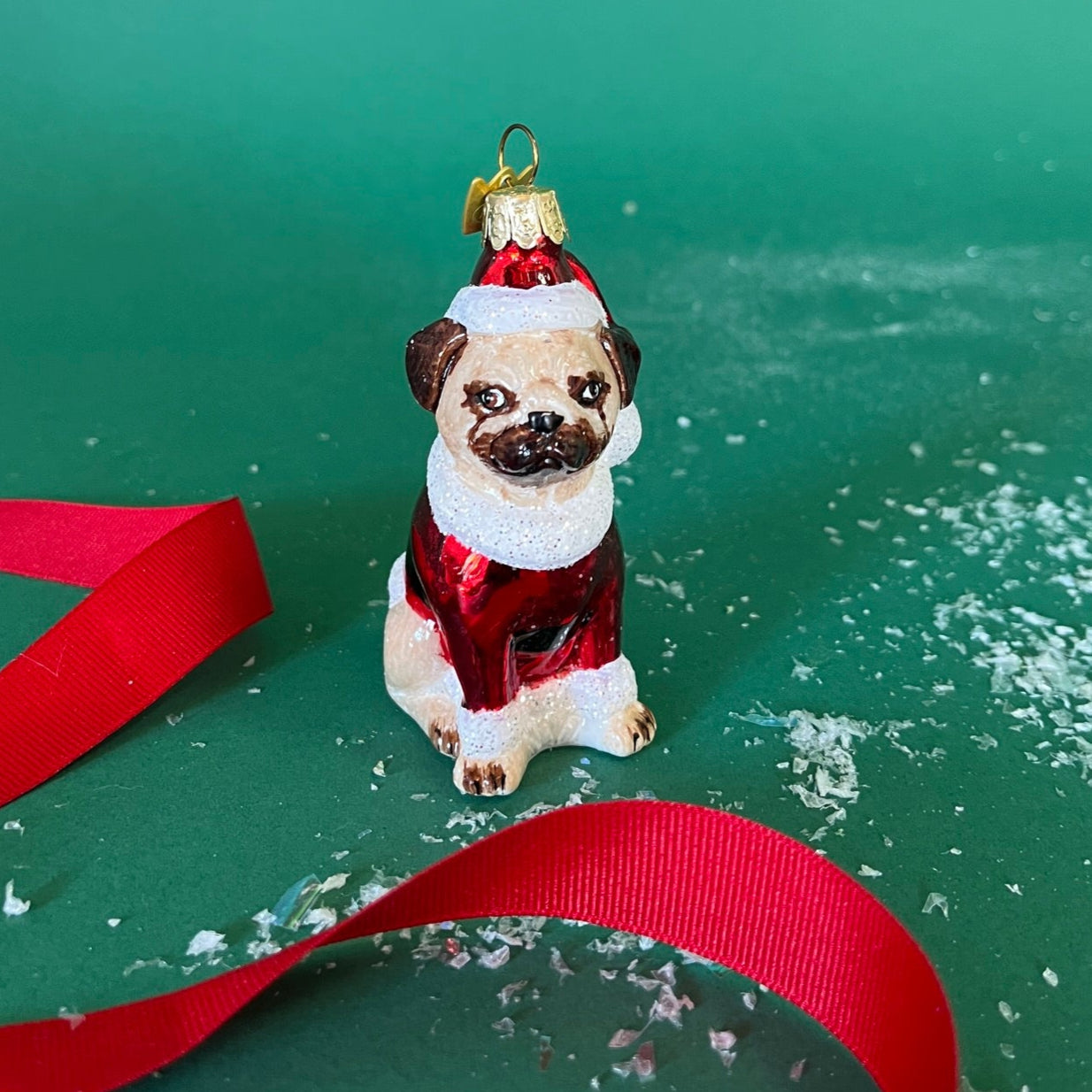 Pug dog ornament in a red outfit with a green background