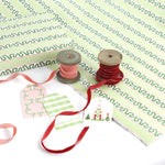 Green striped Christmas wrapping paper roll with gift tags, ribbon spools, and coordinating holiday accessories displayed.