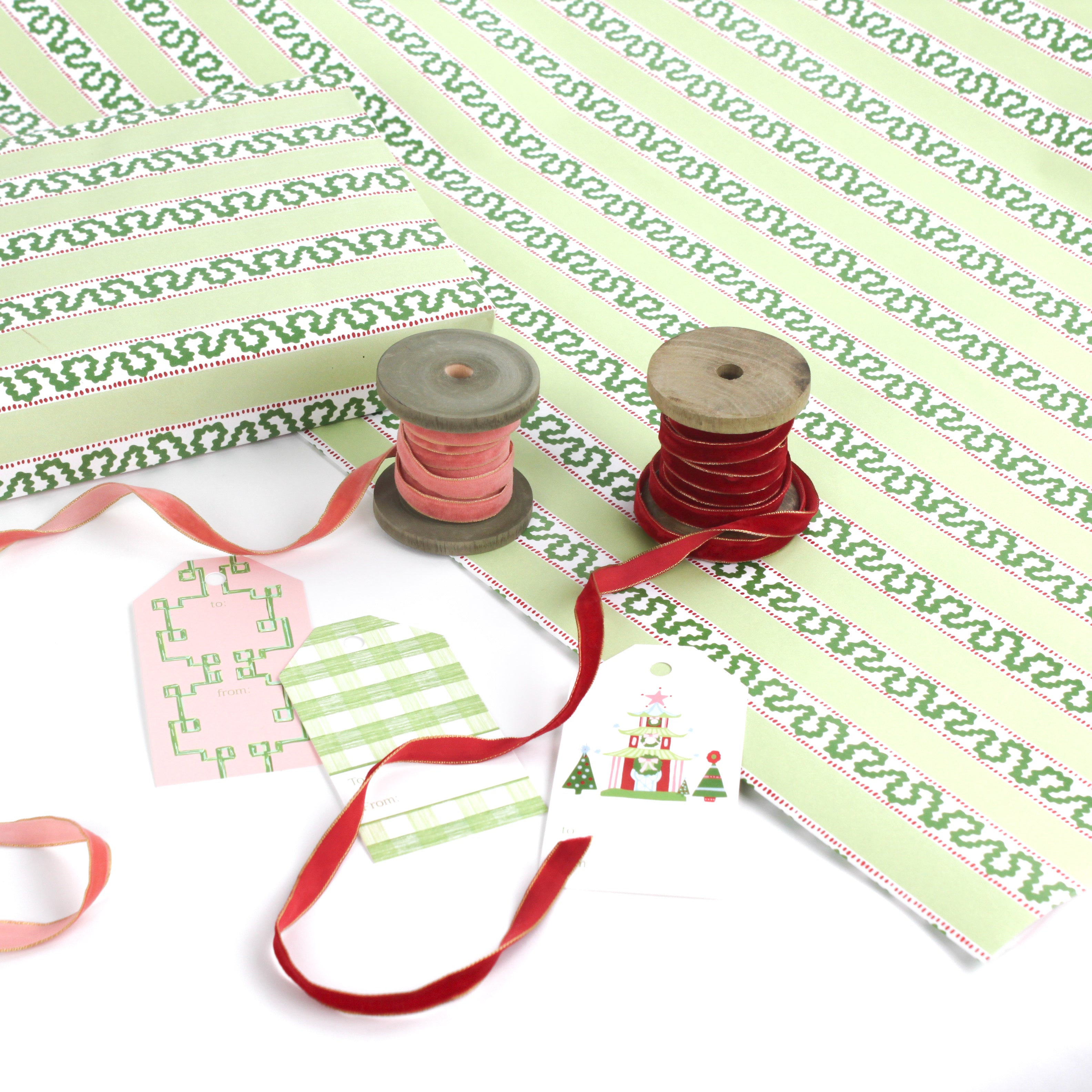 Green striped Christmas wrapping paper roll with gift tags, ribbon spools, and coordinating holiday accessories displayed.