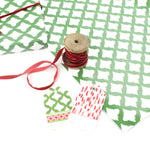 Styled display of green patterned wrapping paper with red ribbon spool and matching gift tags.