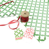 Styled display of green patterned wrapping paper with red ribbon spool and matching gift tags.