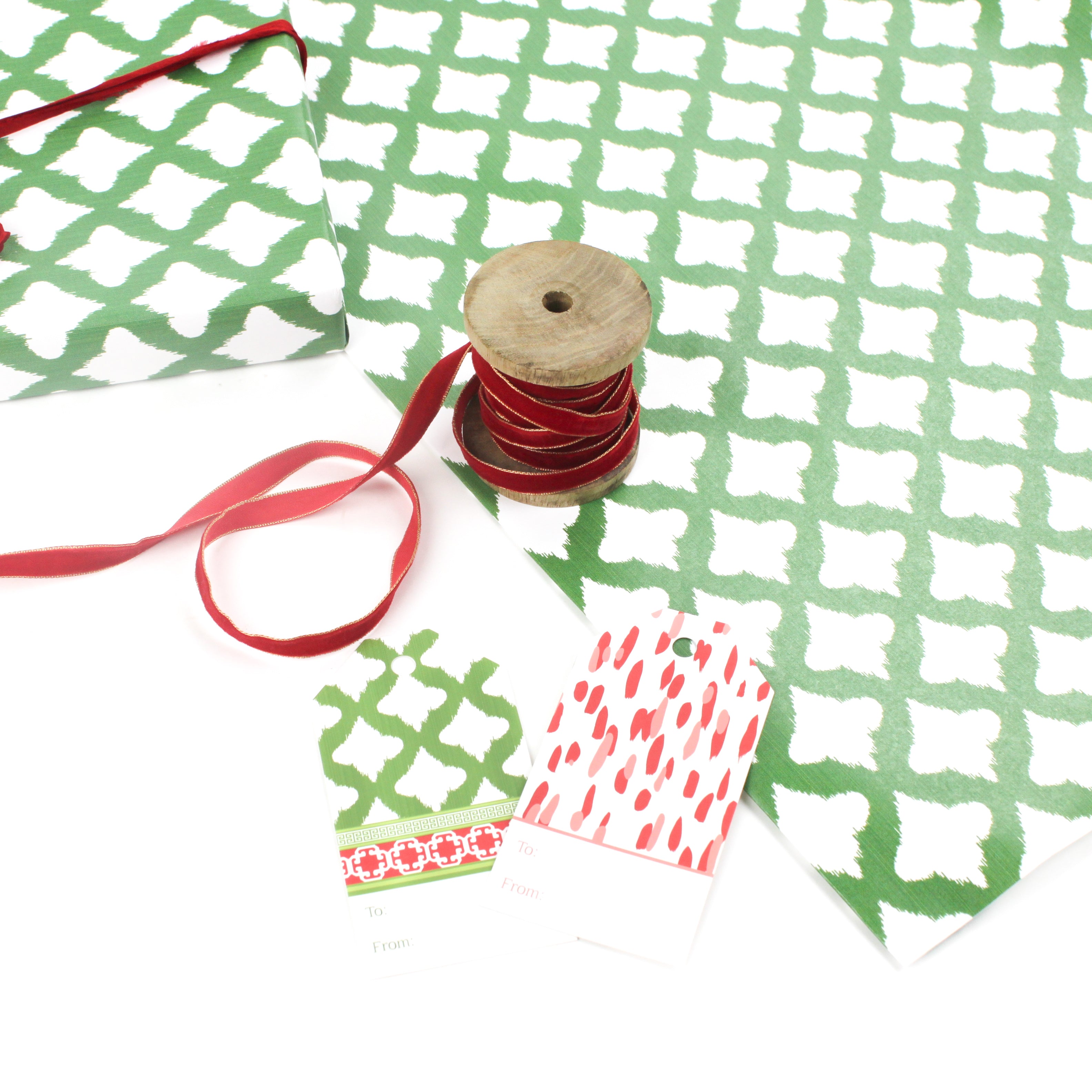 Styled display of green patterned wrapping paper with red ribbon spool and matching gift tags.