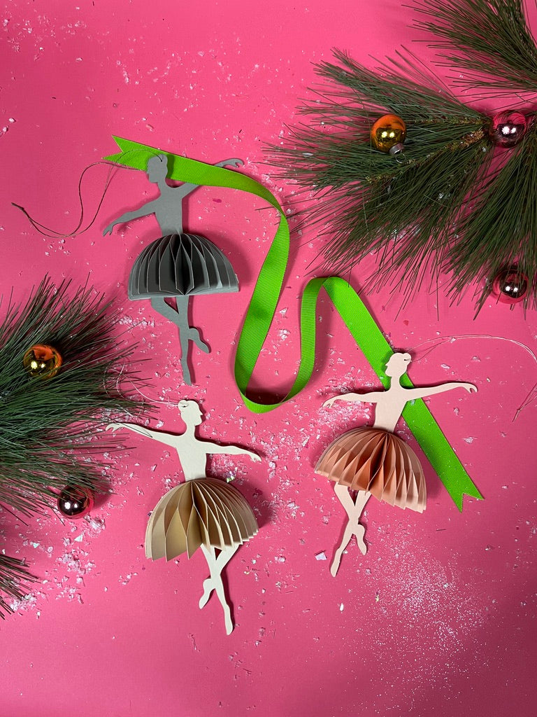 Decorative ballerina ornaments with ribbons and pine branches on a pink background