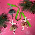 Decorative ballerina ornaments with ribbons and pine branches on a pink background