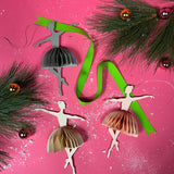 Decorative ballerina ornaments with ribbons and pine branches on a pink background