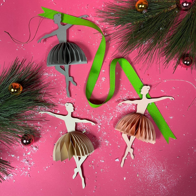Decorative ballerina ornaments with ribbons and pine branches on a pink background