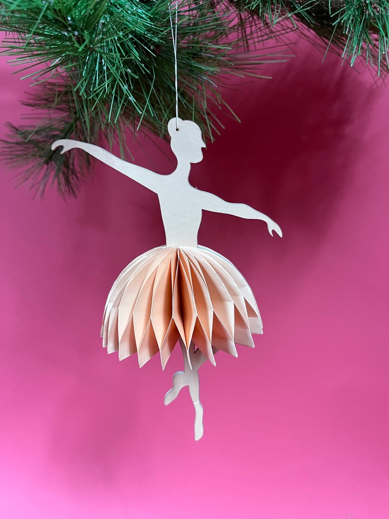 Decorative paper ballerina christmas ornament hanging against a pink background