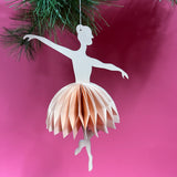 Decorative paper ballerina christmas ornament hanging against a pink background