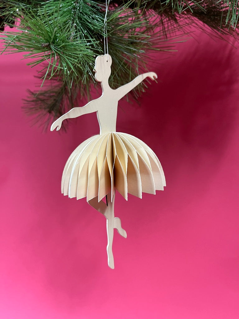 Paper ballerina ornament hanging on a Christmas tree with a pink background