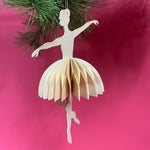 Paper ballerina ornament hanging on a Christmas tree with a pink background