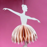 Decorative paper ballerina christmas ornament hanging against a pink background