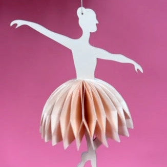 Decorative paper ballerina christmas ornament hanging against a pink background