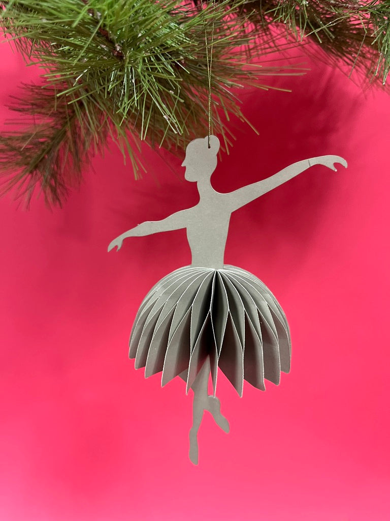 3D ballerina christmas ornament hanging from a Christmas tree branch against a red background