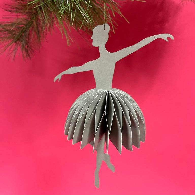 3D ballerina christmas ornament hanging from a Christmas tree branch against a red background
