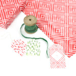 Red geometric gift wrap styled with green ribbon, wooden spools, and assorted gift tags.