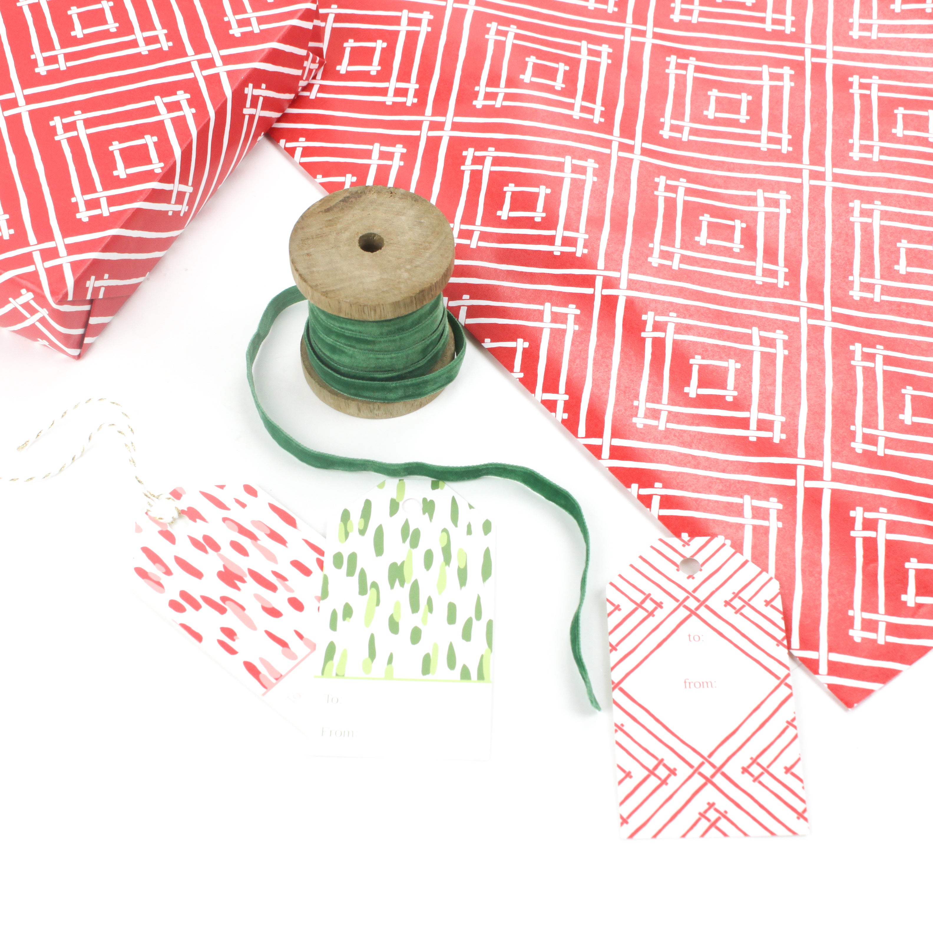 Red geometric gift wrap styled with green ribbon, wooden spools, and assorted gift tags.