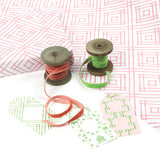 Styled flat lay of Island House Southampton pink wrapping paper with hand-drawn trellis pattern, paired with green and coral velvet ribbon on wooden spools and coordinating gift tags.