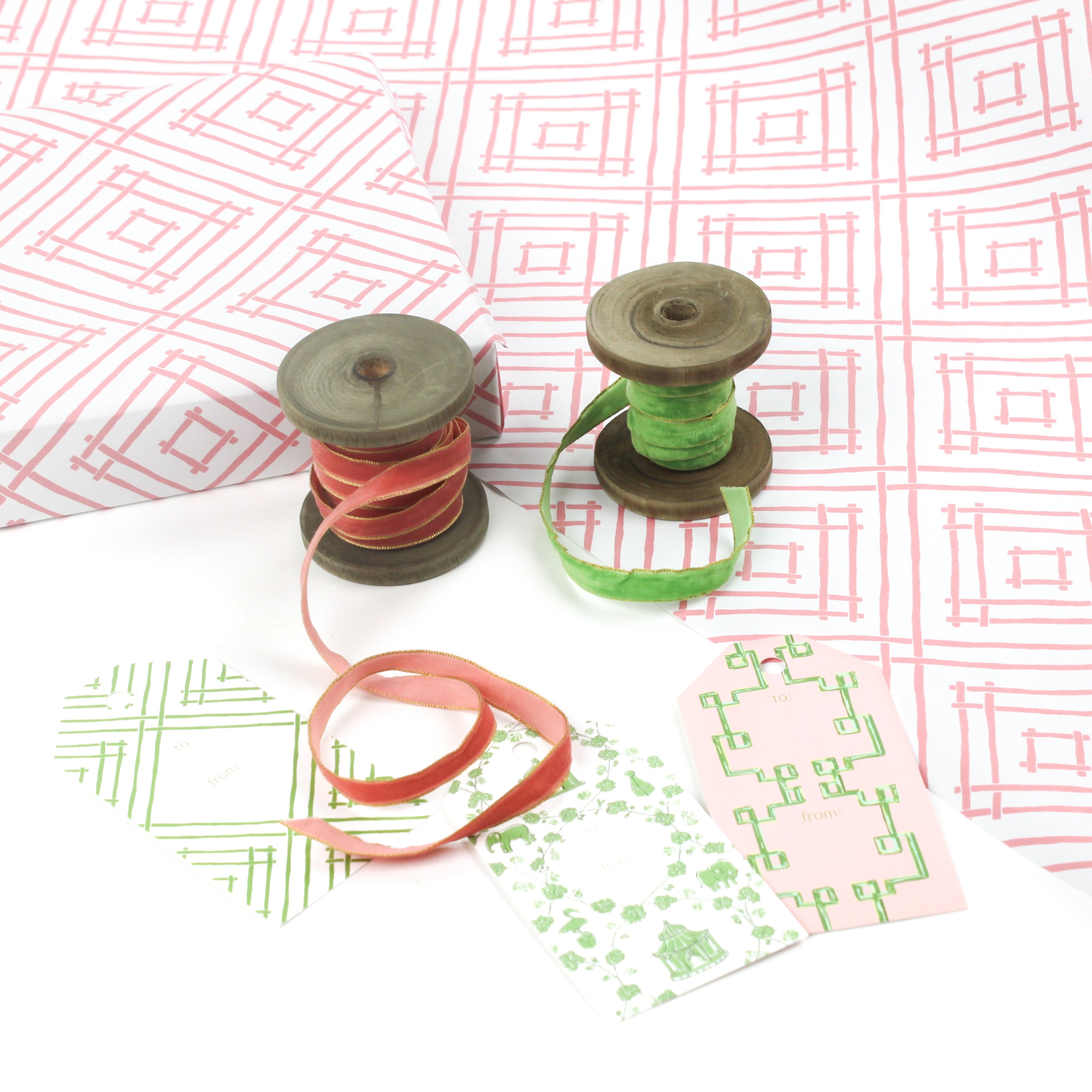 Styled flat lay of Island House Southampton pink wrapping paper with hand-drawn trellis pattern, paired with green and coral velvet ribbon on wooden spools and coordinating gift tags.