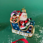 Santa Sleigh Glass Christmas Ornament in a green background