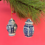 Two blue and white ginger jar ornaments hanging from a Christmas tree branch against a red background.