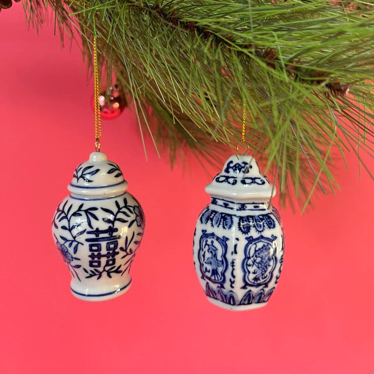 Two blue and white ginger jar ornaments hanging from a Christmas tree branch against a red background.