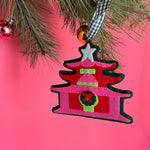 Decorative chinoiserie Christmas ornament shaped like a pagoda with a star on top, hanging from a tree branch against a pink background.