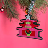 Decorative chinoiserie Christmas ornament shaped like a pagoda with a star on top, hanging from a tree branch against a pink background.