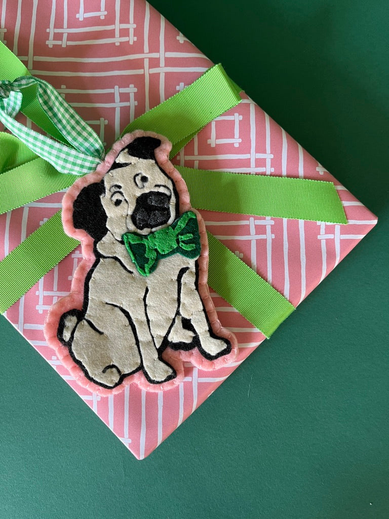 Pug ornament with a green bow tie on a pink and white patterned gift with a green ribbon.